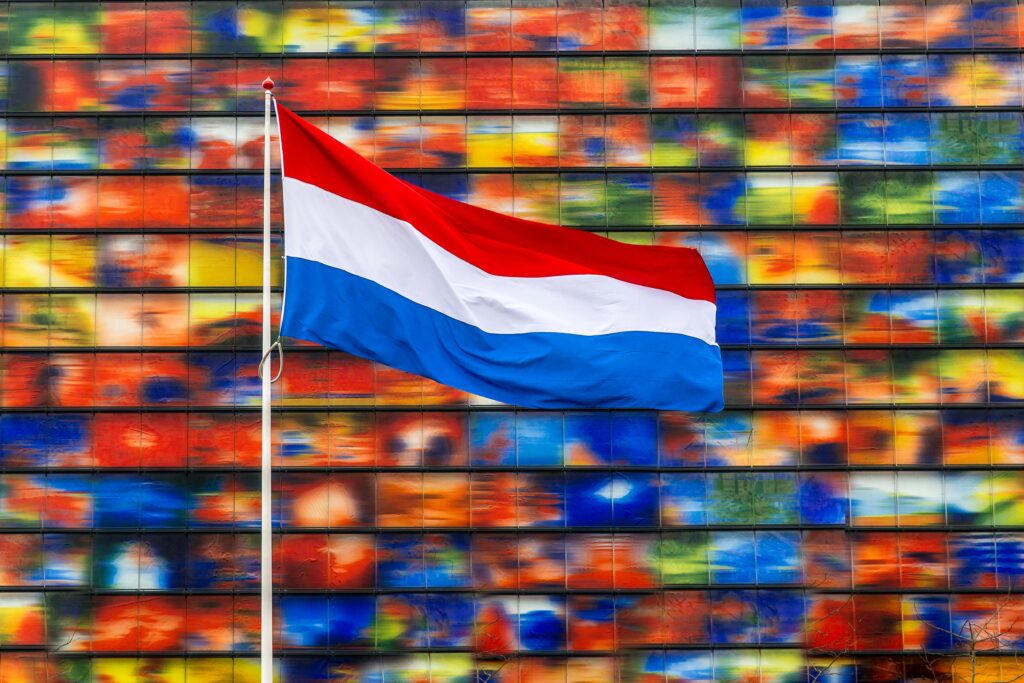 Dutch flag waving in front of a vibrant, colorful building facade in the Netherlands.